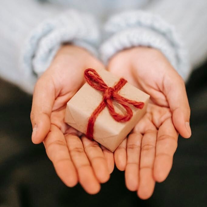 High angle crop unrecognizable female in blue sweater demonstrating small wrapped present box on hands